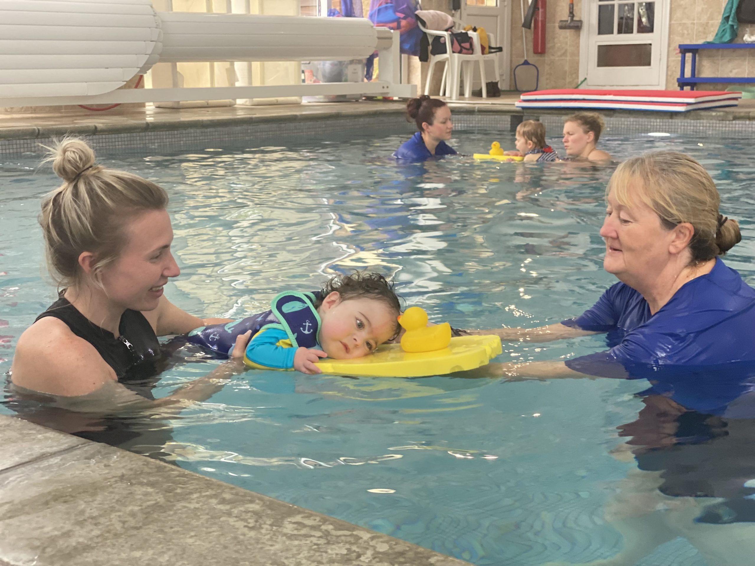 A young boy in a swimming pool with a carer and swimming instructor.