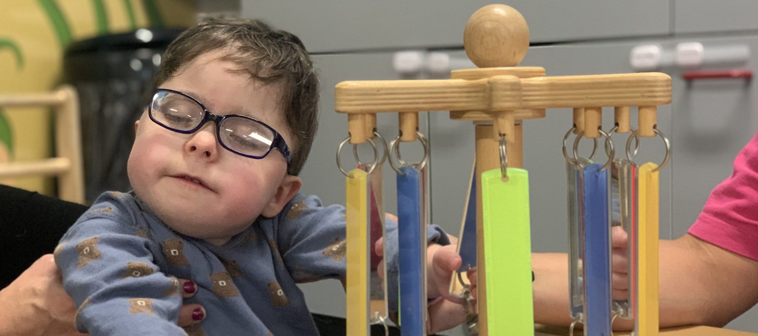 A young boy with Bohring-Optiz Syndrome playing with a toy in a conductive education session.