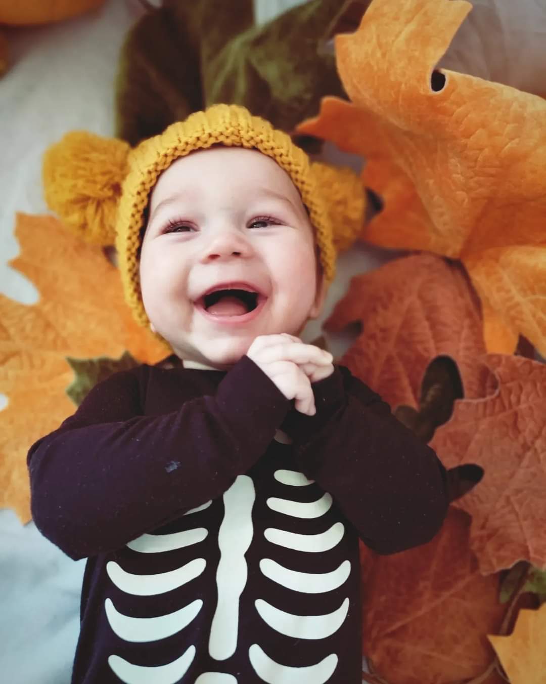 A young baby laying on a bed of autumn leaves.