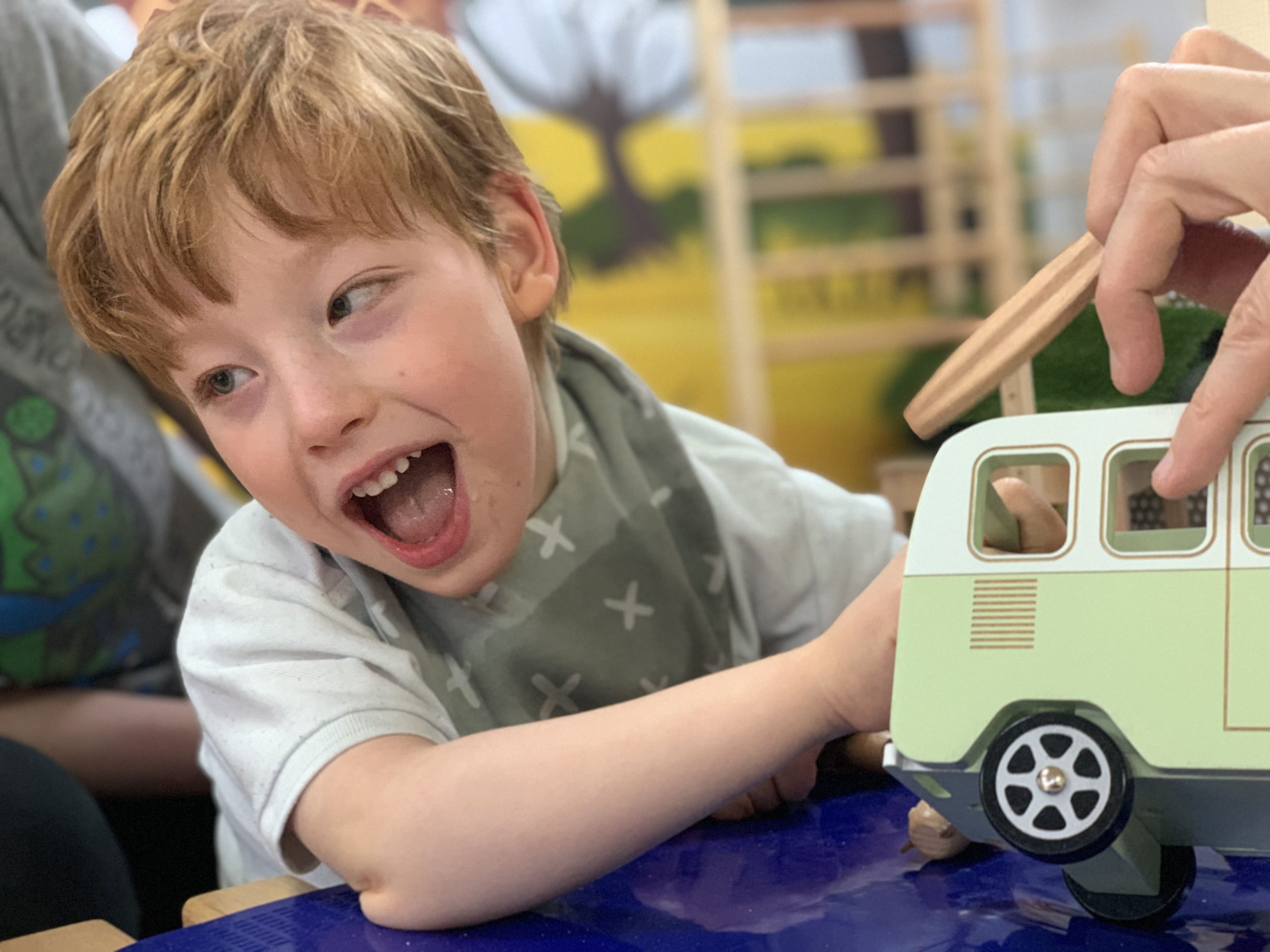 A young boy with cerebral palsy playing with a toy campervan.